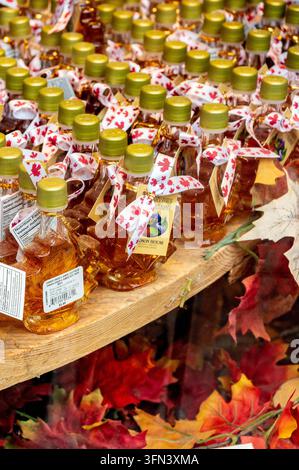 File di sciroppo d'acero puro in bottiglie di vetro a forma di foglia d'acero decorate con nastri e foglie autunnali in un negozio di souvenir. Foto Stock