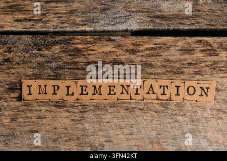 Striscia di carta con la parola "implementazione" stampata con lettere da timbro su una texture di legno rustico Foto Stock