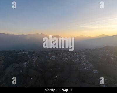 Panorama aereo con drone che cattura il villaggio di Cemoro Lawang, montagne vulcaniche, terreni agricoli e valli nebbiose sotto un tramonto luminoso nell'est di Giava. Foto Stock