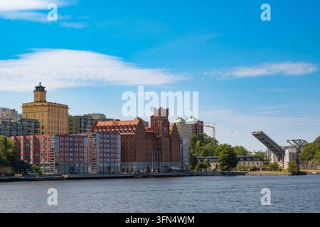 Vista grandangolare dell'edificio storico del mulino di Saltsjoqvarn in mattoni rossi, della torre gialla simbolo, degli appartamenti moderni sul lungofiume e del ponte basculante Danviksbron Foto Stock