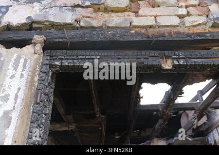 Travi di legno bruciate e muratura carbonizzata rivelano una struttura residenziale devastata dopo un incendio, mostrando muri distrutti, struttura esposta e il netto a Foto Stock