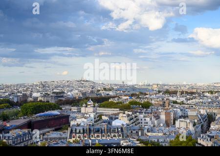 Silhouette di Parigi sotto un vasto cielo parzialmente nuvoloso. Le linee dei tetti si estendono attraverso i quartieri storici della città. Torri, cupole e camini si ergono dalla densità Foto Stock