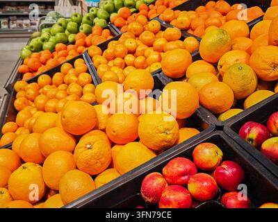 I clienti visitano un supermercato per selezionare frutti freschi come arance e mele dalle esposizioni ordinate per i loro pasti Foto Stock