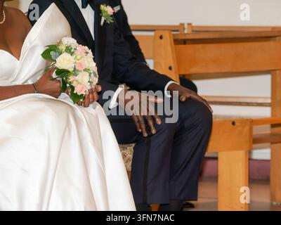 Sposa in abito da sposa bianco con bouquet e sposo in abito scuro seduti su una panchina durante la cerimonia Foto Stock
