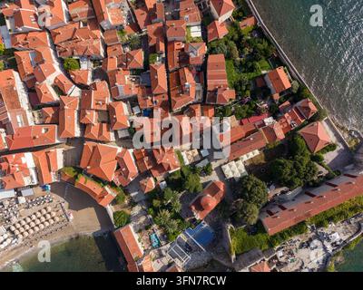 Budva in Montenegro appare dal sopra mentre i tetti fitti della vecchia città incontrano il mare Adriatico scintillante. Edifici con tetti di tegole rosse, vicoli stretti e lungomare ombreggiato Foto Stock