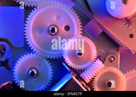 Vista macro di ingranaggi di plastica bianca all'interno di un dispositivo illuminato con luce neon blu e rosa. Meccanismo industriale con illuminazione sfumata vivace. Foto Stock