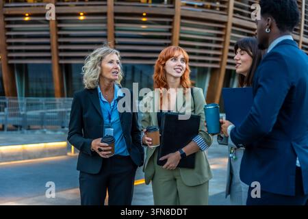 Diversi colleghi di lavoro in piedi su una strada cittadina, chiacchierando con un caffè durante una pausa, facendo networking e discutendo di lavoro, piani e lavoro di squadra in prof Foto Stock