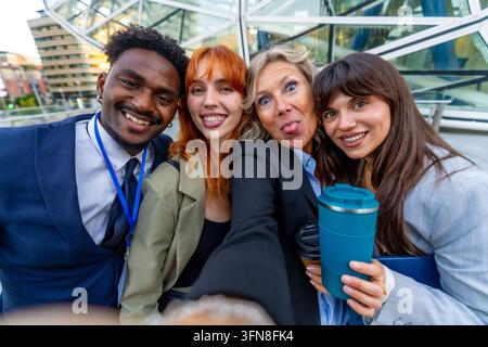 Diversi colleghi di lavoro che creano legami e si divertono all'aperto, catturando un momento memorabile con un selfie di gruppo, celebrando il lavoro di squadra e l'amicizia in Foto Stock