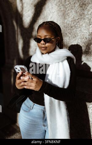 Donna elegante con trecce che usa il suo smartphone all'aperto Foto Stock