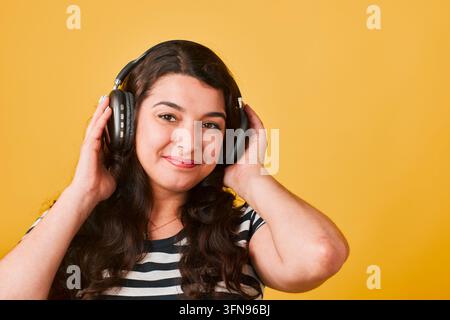 Giovane donna felice con cuffie che ascolta musica su uno sfondo giallo brillante Foto Stock