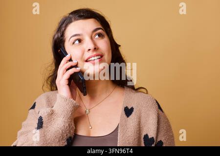Giovane donna che parla al telefono con espressione felice indossando un cardigan a forma di cuore, ritratto casual Foto Stock