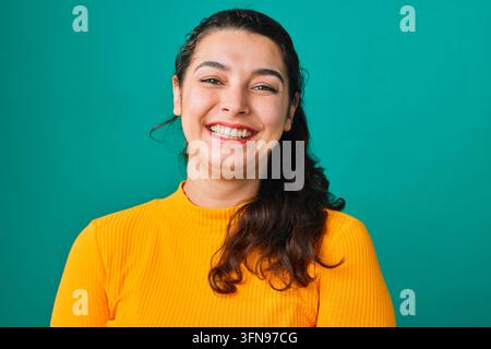 Giovane donna sorridente in maglione giallo, ritratto su sfondo verde-azzurro che trasmette gioia e sicurezza Foto Stock