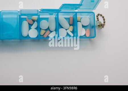 Organizer giornaliero in plastica blu con varie pillole e farmaci all'interno su sfondo bianco. Scomparti aperti con compresse e capsule mediche. Foto Stock