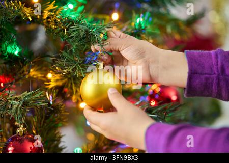 Natale, ornamento e mani di una ragazza con decorazione dell'albero durante le vacanze o in casa. Festoso, celebrazione e primo piano con pallina di vetro per Natale Foto Stock