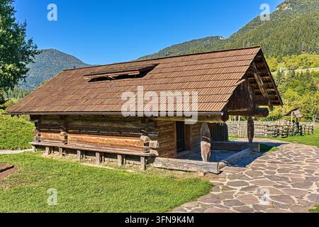 Capanna tradizionale in tronchi di legno con tetto di scandole e sentiero di pietra sotto le montagne. Foto Stock