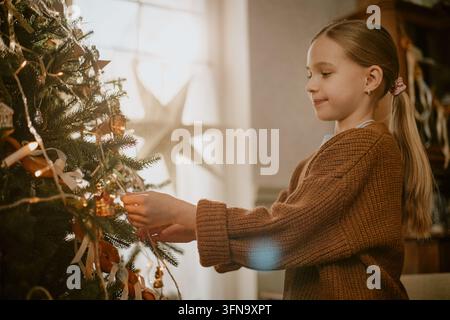 Bambina carina che decora l'albero di Natale a casa per le feste Foto Stock