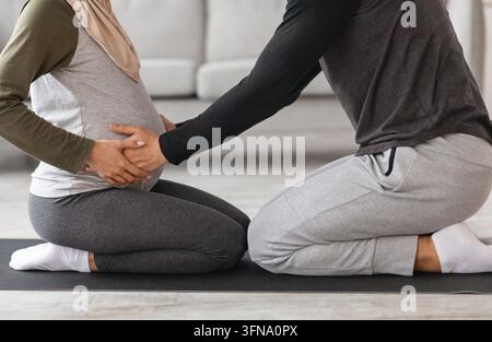 Coppie gravidanza Yoga. Cropped Shot di coniugi musulmani formazione insieme a casa Foto Stock