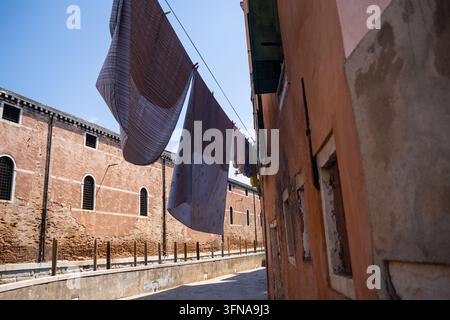 Vista di biancheria appesa a una corda tra edifici storici in mattoni in un vicolo stretto a Venezia, Veneto, Italia. Foto Stock