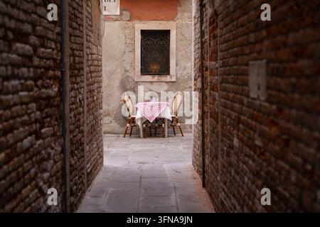 Vista di un piccolo tavolo con due sedie apparecchiate per la cena in un vicolo stretto di mattoni a Venezia, Veneto, Italia. Foto Stock