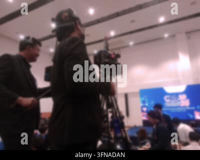 Squadra di produzione video professionale che filma un evento indoor con una telecamera su treppiede, rappresentante la produzione multimediale, la videografia, la radiodiffusione, il journali Foto Stock