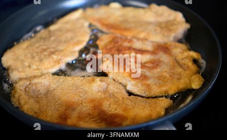 Costolette di carne impanate croccanti che cuociono e sfrigolano in una padella con olio Foto Stock