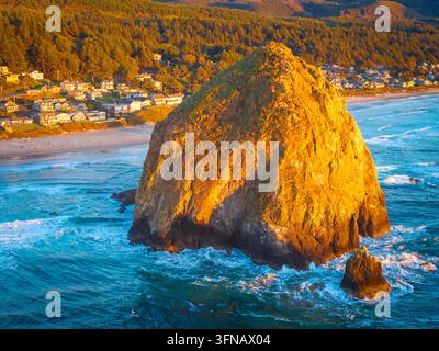 Una vista aerea mozzafiato di Haystack Rock e della costa di Cannon Beach, immersa nella calda e dorata luce di un vibrante tramonto sull'Oceano Pacifico Foto Stock