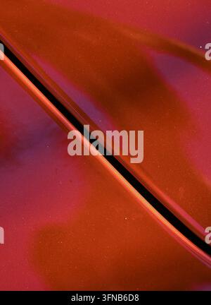 Fotografia verticale dettagliata di una superficie metallica della carrozzeria dipinta di un rame-arancio con una giuntura verticale curva e riflessi morbidi. Foto Stock
