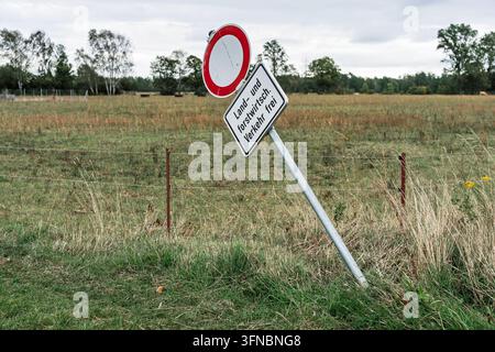 Segnale stradale inclinato con testo tedesco "Land und forstwirtsch Verkehr frei (Traffico agricolo e forestale consentito)" accanto a una recinzione in filo spinato. Foto Stock