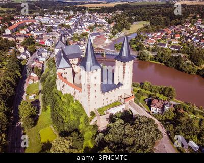 Questa fotografia aerea presenta l'affascinante città di Rochlitz nella Sassonia, Germania, circondata da un paesaggio pittoresco di campi, alberi e campagna ondulata. La prospettiva elevata rivela la struttura urbana storica, le aree residenziali, le strade e Foto Stock