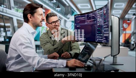 Ingeniero informatico codifica con attenzione una piattaforma sicura utilizzando un laptop alla scrivania. Foto Stock