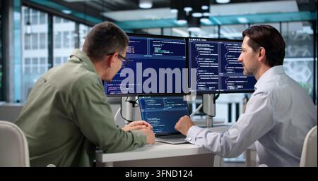 Ingeniero informatico scrive con attenzione algoritmi sicuri alla sua scrivania affollata. Foto Stock