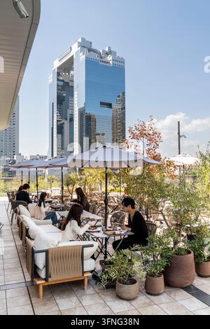 Clienti che mangiano all'aperto in un ristorante sul terrazzo superiore del palazzo Umekita Green Place con il landmark Umeda Sky Building sullo sfondo. Cielo azzurro. Foto Stock
