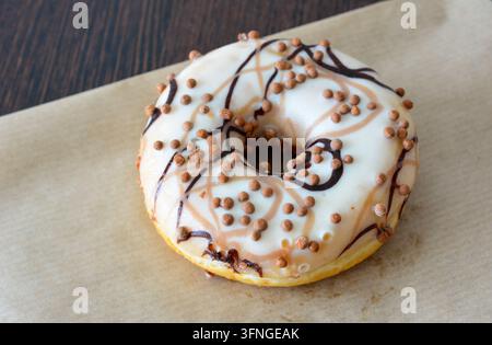 Donut glassato con gocce di cioccolato su carta pergamena, macro, spazio di copia Foto Stock