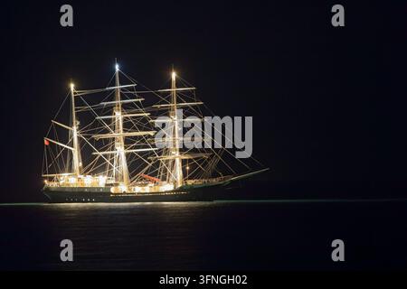 La nave a tre alberi britannica SV Tenacious ancorata in mare, i suoi alberi, l'attrezzatura e il ponte splendidamente illuminati contro il cielo notturno scuro. Foto Stock