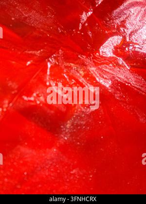 Superficie di liquido viscoso rosso acceso con piccole bolle e riflessi. Dettaglio di texture alimentare astratta, finitura lucida, vista macro ideale per sfondo Foto Stock