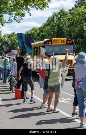 Saint Paul, Minnesota, USA - 17 luglio 2025: i manifestanti alzano i pugni e i cartelli mentre un autobus scolastico giallo passa durante una protesta di strada anti-Trump in pieno sole. Foto Stock