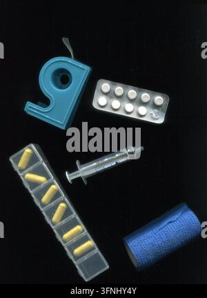 Una striscia di pillole bianche, una benda, un rotolo di bende, una siringa e un organizzatore di pillole su sfondo nero; scansione di forniture mediche Foto Stock