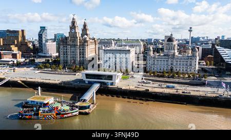 Vista aerea con drone del lungomare di Liverpool in Inghilterra, che mostra il Royal Liver Building, il Port of Liverpool Building e una colorata nave traghetto sul Ri Foto Stock