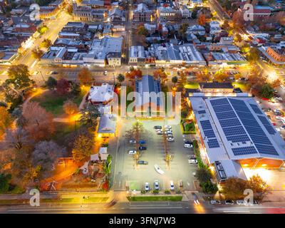 Vista aerea di Castlemaine, Victoria, Australia, al crepuscolo, che mostra strade cittadine illuminate, edifici storici, parcheggi e tetti circostanti Foto Stock
