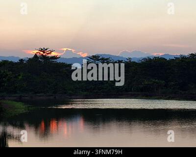 Bellissimo tramonto su un lago calmo con silhouette di montagne e riflessi di alberi sulla superficie dell'acqua, sfondo di paesaggio tropicale tranquillo Foto Stock