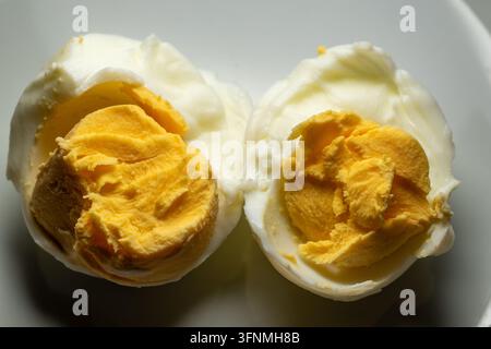Prima vista di un uovo sodo tagliato a metà che mostra il tuorlo giallo solido e l'albume cotto su un piatto Foto Stock