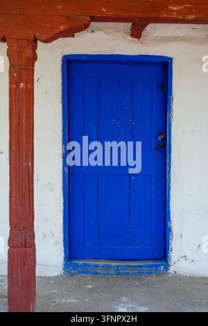 Porta tradizionale in legno blu di una vecchia casa rustica all'interno di un museo del villaggio storico con pareti imbiancate a calce e una colonna in legno intagliato Foto Stock