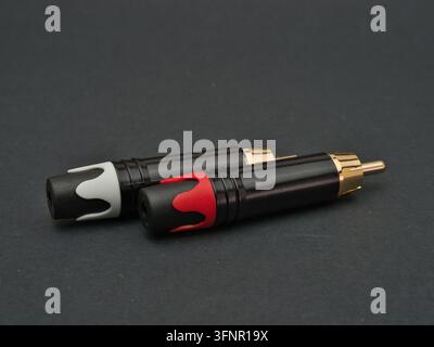 Due connettori RCA su sfondo scuro - Due connettori audio RCA, uno con un accento rosso e l'altro con un accento bianco, sono disposti su una superficie grigio scuro, hig Foto Stock