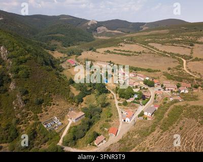 Veduta aerea che mostra un villaggio remoto circondato da montagne e colline sotto un cielo estivo Foto Stock