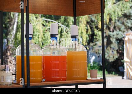 Distributori trasparenti contengono bevande ai frutti arancioni e rossi sotto un ombreggiato tendone di mercato all'aperto. Foto Stock