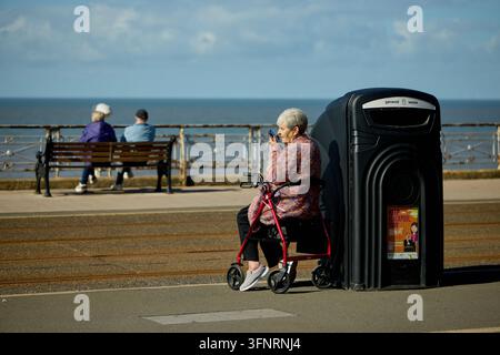 Signora in pensione sulla passeggiata di Blackpool che si riposa sul suo bastone da passeggio Foto Stock
