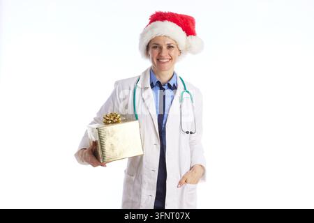 Una medico indossa un cappello da Babbo Natale e tiene una scatola regalo d'oro, rappresentando la professionalità medica mescolata al calore delle festività e al benessere stagionale. Foto Stock
