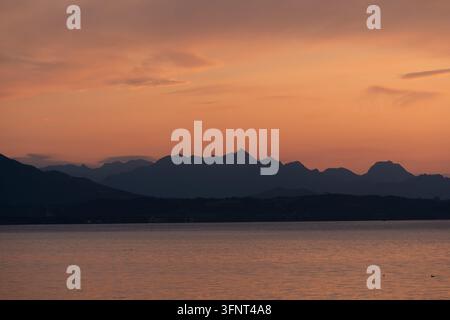 Vista sul lago Chiemsee da Chieming verso il monte Wendelstein e le Alpi bavaresi al tramonto, con la silhouette distintiva della trasmittente sulla cima Foto Stock