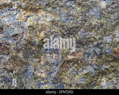 Superficie di pietra ruvida e consumata con crescita naturale di licheni e depositi minerali ossidati in una vista macro a distanza ravvicinata che mostra la trama dettagliata della roccia Foto Stock