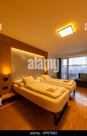 Camera d'albergo moderna con illuminazione ambientale calda, due letti singoli comodi e dettagli in legno Foto Stock
